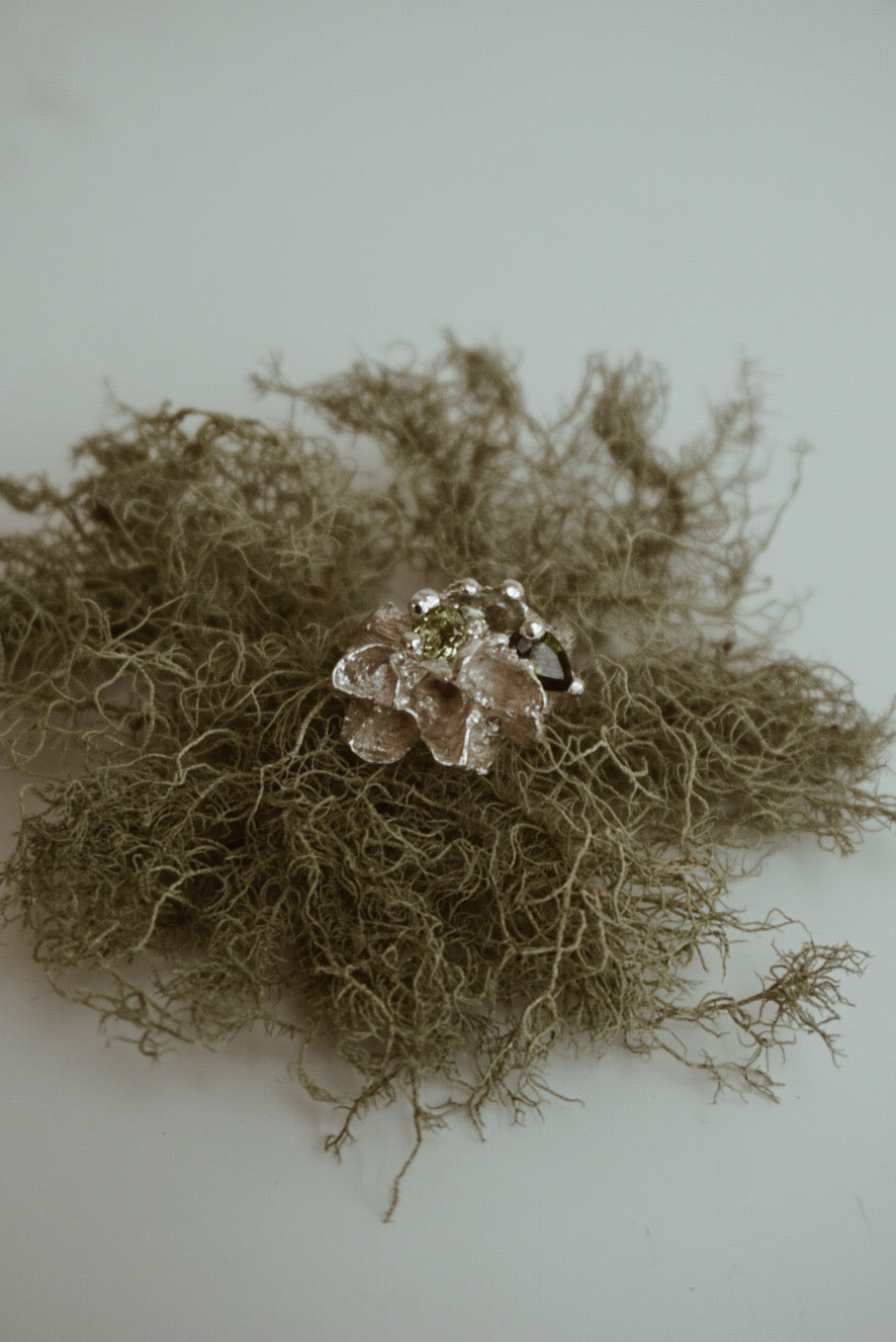 Silver ring with green gemstones on a textured surface with a neutral background