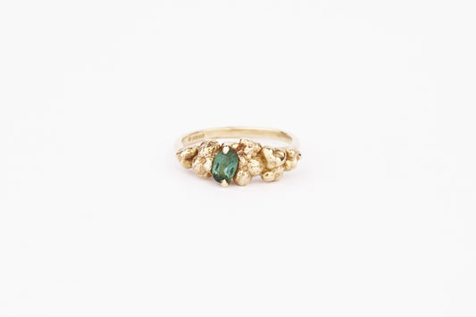 A gold-colored open band ring with a hand-carved design featuring oval dark green tourmaline, set in a metal band.